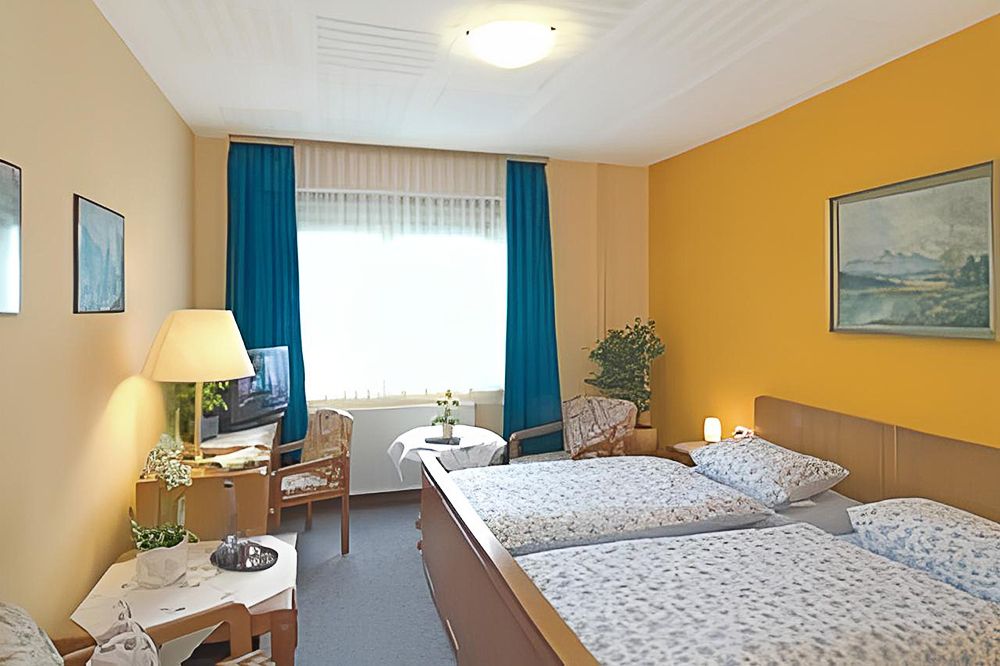 Zimmer mit Doppelbett im rustikalem Stil, die Wände sind gelb gestrichen und die Vorhänge blau
